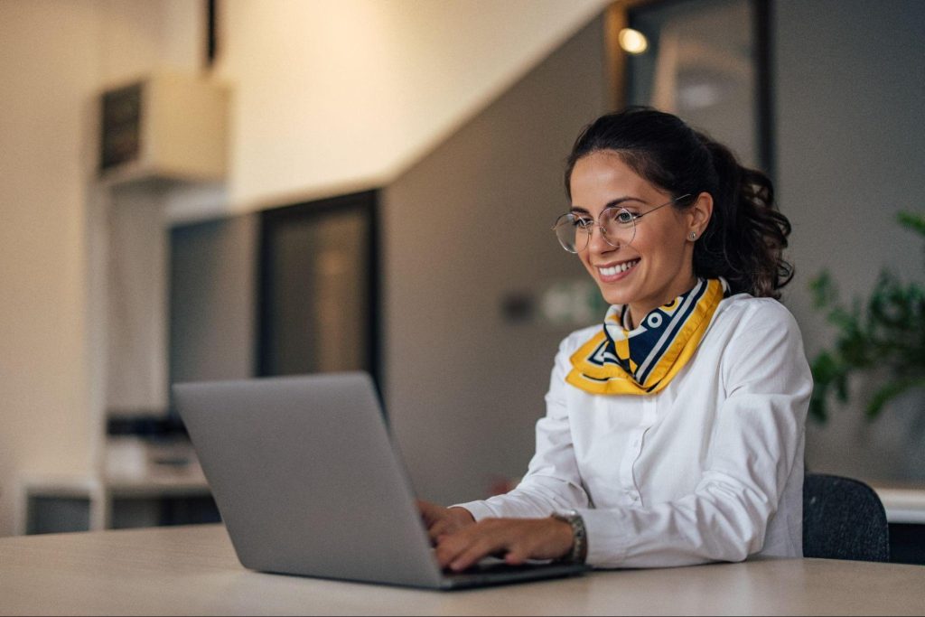 Mujer sonriente usando su laptop en una oficina para firmar un contrato con firma electrónica de forma rápida y segura